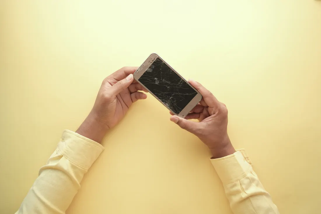 Stock photograph of a person holding a phone with a broken screen